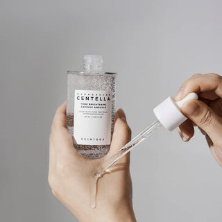 A close-up of SKIN1004's Madagascar Centella Tone Brightening Capsule Ampoule being dispensed onto the back of the hand, showcasing its essence-like texture.
