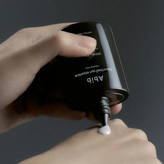 Close-up of Abib's Heartleaf Sun Essence Calming Drop SPF 50+ PA++++ being dispensed onto the back of the model's hand, revealing its runny, milky texture.
