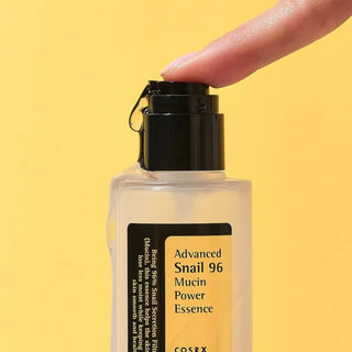 Close-up of a model's finger pressing the pump of COSRX's Advanced Snail Mucin Essence, with the product being dispensed.