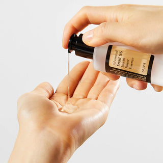 Close-up of COSRX's Advanced Snail Mucin Essence being dispensed onto a model's hand, showing its thick gel texture.
