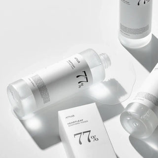 Anua's Heartleaf Toner with the cap off, showing the product spilling out through a small opening. The texture is water-like and lightweight.