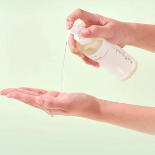 A close-up of Anua's Heartleaf Pore Control Cleansing Oil being dispensed onto the model's hand.