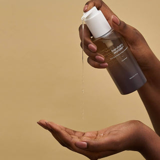 A close-up of haruharu wonder's Wonder Black Rice Moisture Deep Cleansing Oil being dispensed onto the model’s hand, highlighting its smooth, medium-textured consistency.